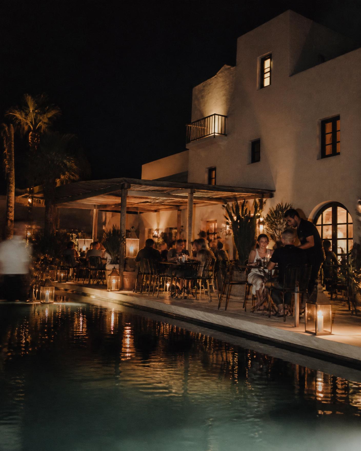 Hotel terrace at night with candlelit tables beside a pool
